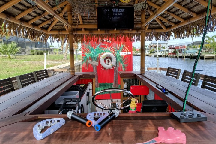 Tiki-themed boat bar with stools, tropical decor, and a waterfront view.