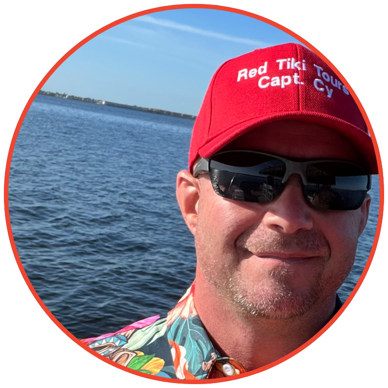 Person in red hat and sunglasses by water, wearing a colorful shirt.