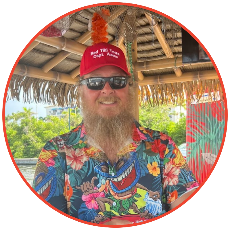 Smiling person in colorful shirt and red hat under tiki roof.