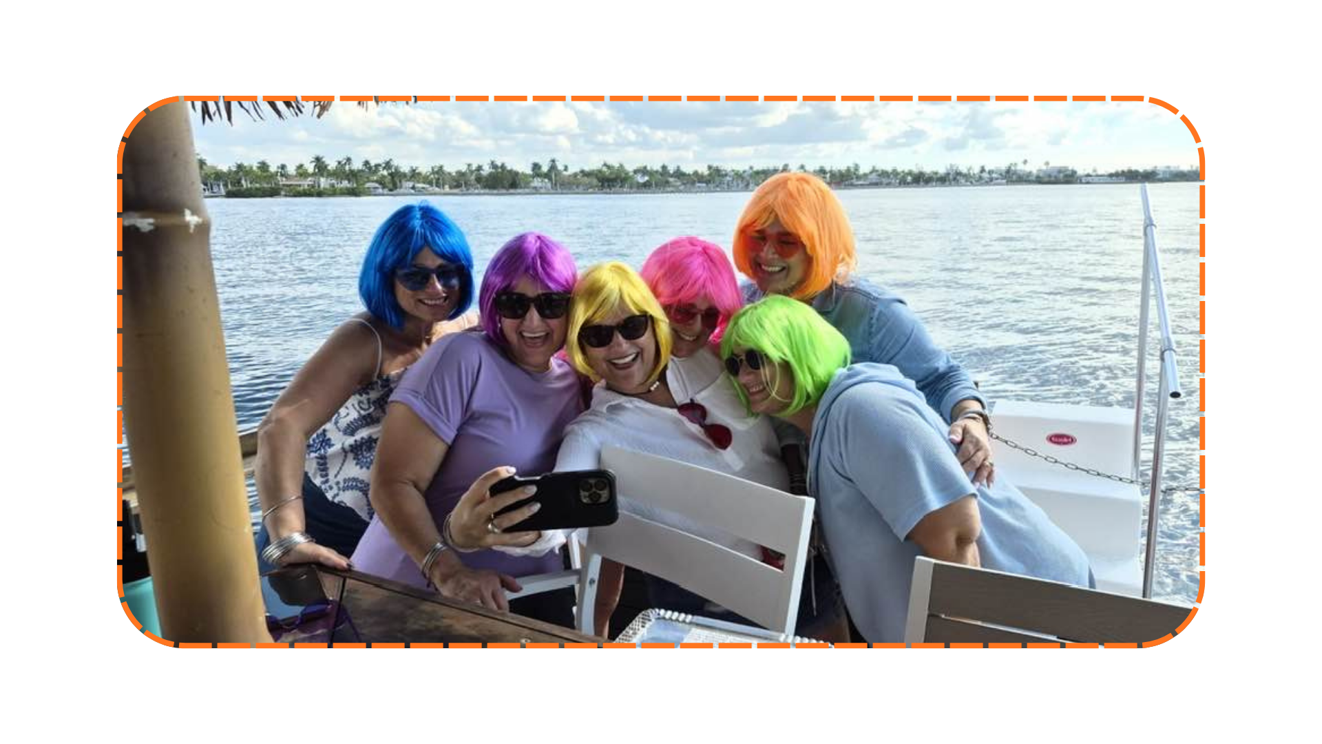 Six people in colorful wigs taking a selfie by the water.
