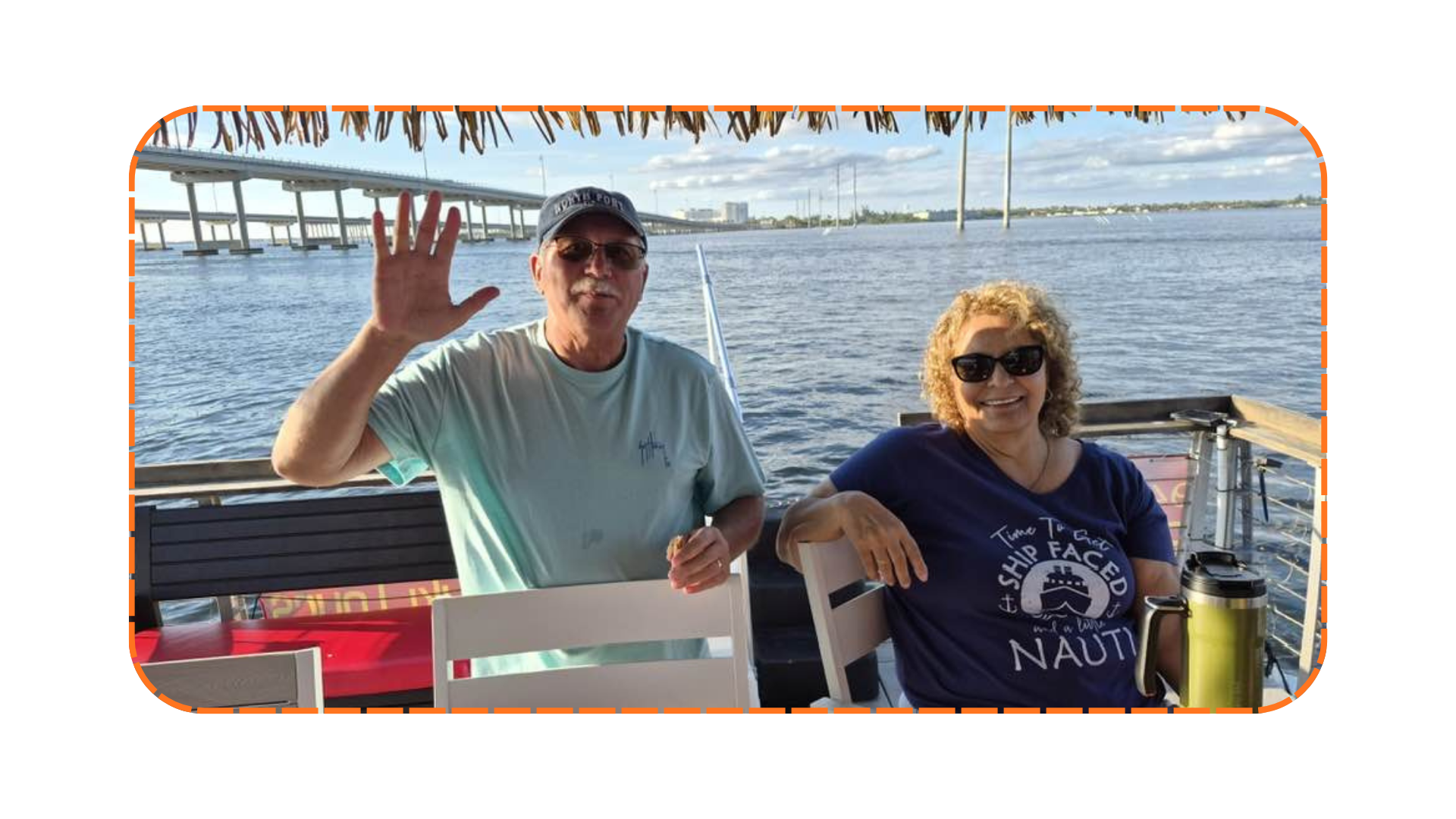 Two people on a boat; man waving, woman seated, bridge and water in background.