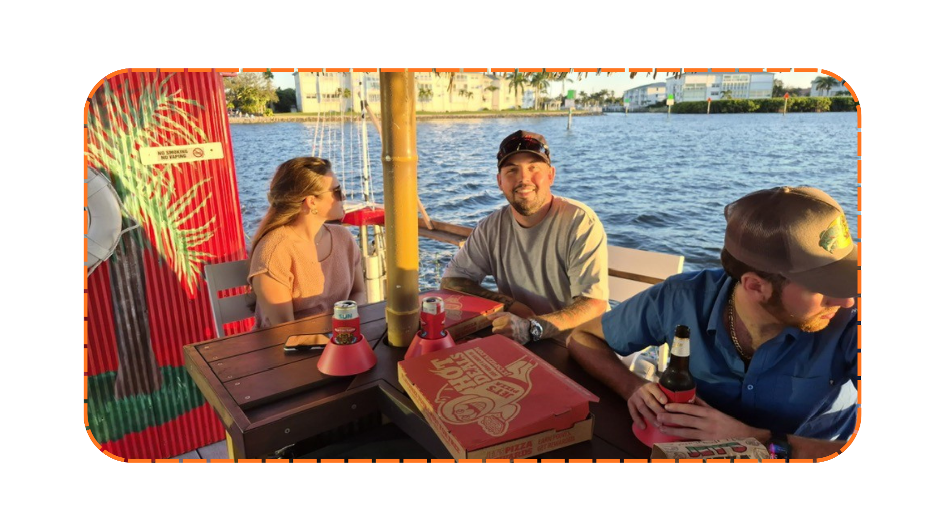 Three people enjoying food and drinks on a boat by the water.